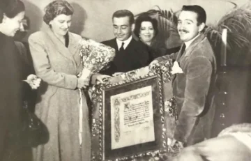 A group of people holding a framed diploma and a bouquet of flowers, in a historic photograph.