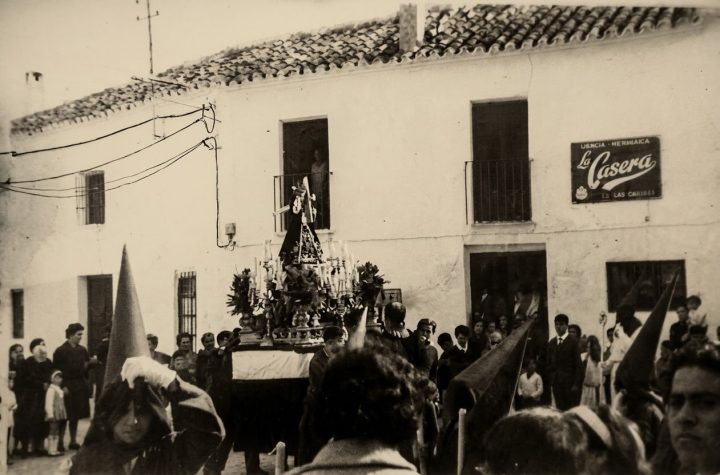 El trono del Dulce Nombre de Jesús entre sus nazarenos de capirote, ante las casas encaladas, en una fotografía antigua