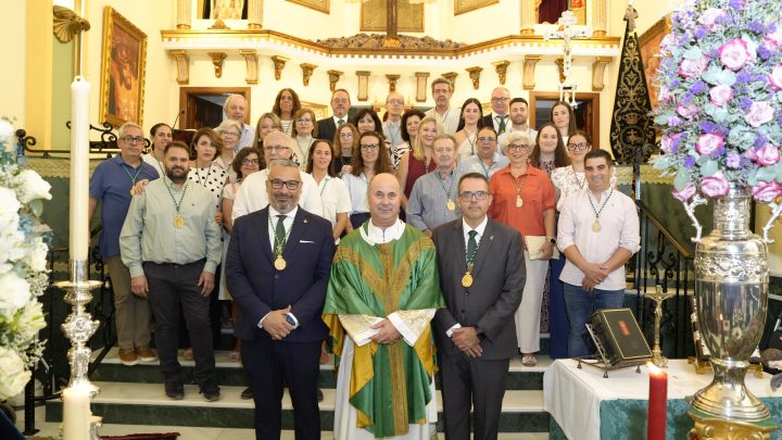Hermanos y hermanas de la Vera+Cruz con sus medallas, junto al sacerdote, ante el altar de la iglesia