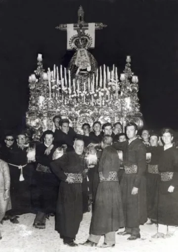 María Santísima de las Angustias on her trono at night, surrounded by brotherhood members, in a historic photograph.