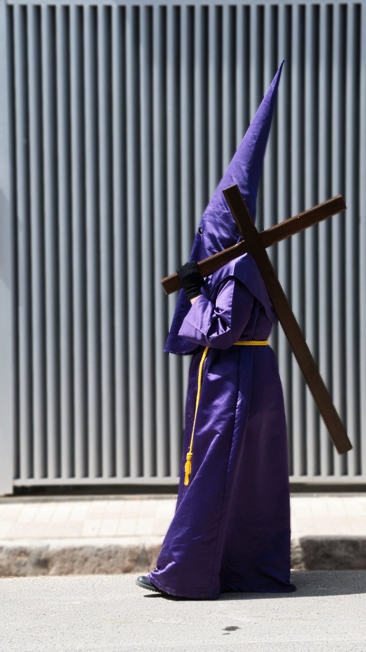 Penitente de Jesús Nazareno con túnica morada y cruz al hombro