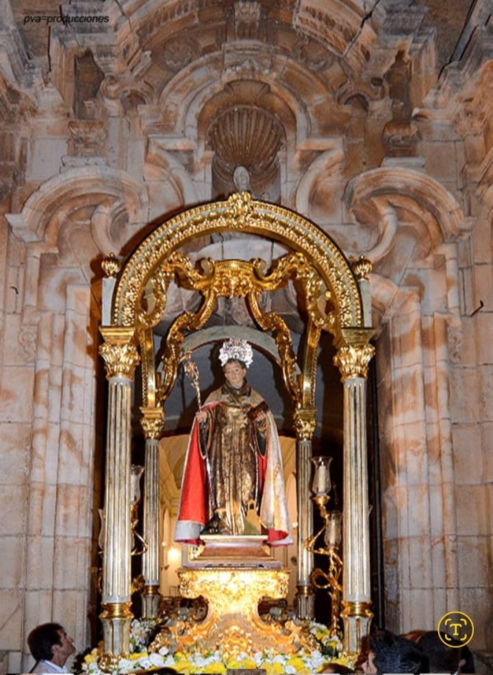 San Benito Abad bajo su templete dorado, con capa roja, ante una portada barroca de piedra