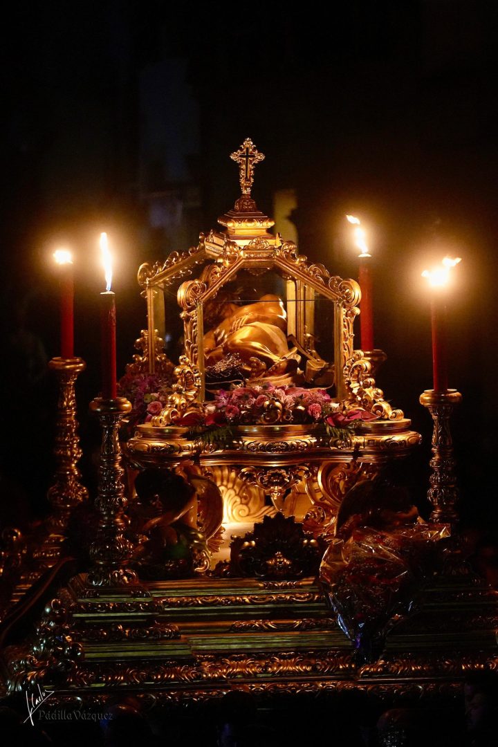 La urna del Santo Entierro de Cristo en su trono, alumbrada por cirios rojos en la noche