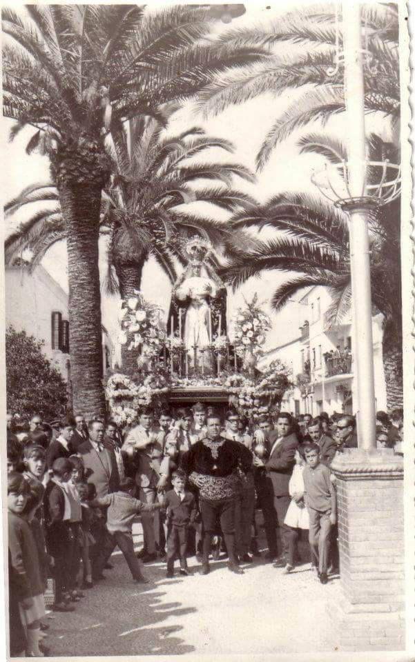 La Virgen del Socorro en su trono por la Plaza de España, entre las palmeras y el público, en una fotografía antigua